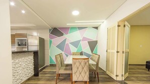 A dining area with a geometric-patterned wall, a modern kitchen in the background, and a door leading to another room.