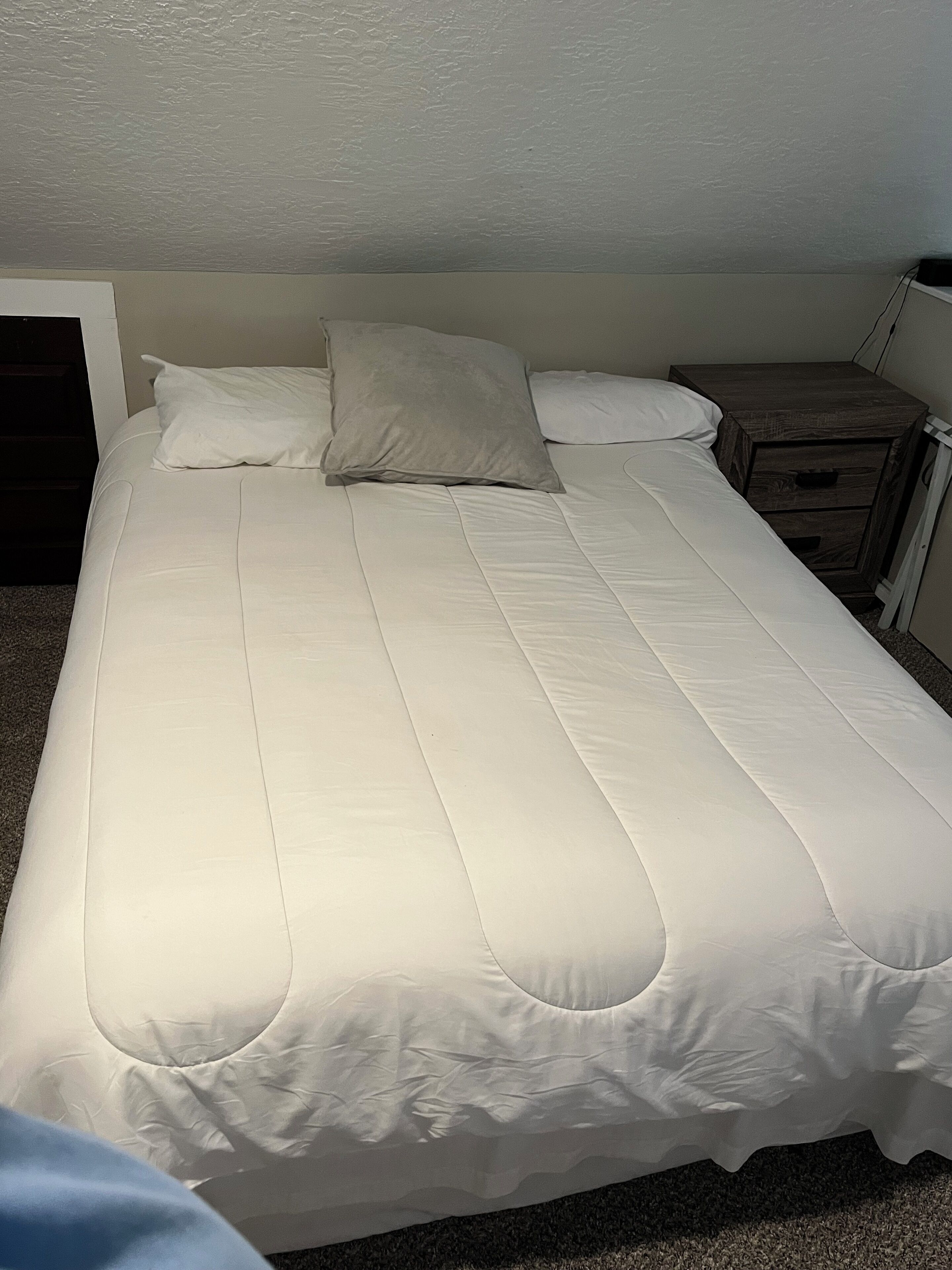 A neatly made bed with white bedding and a wooden nightstand beside it.