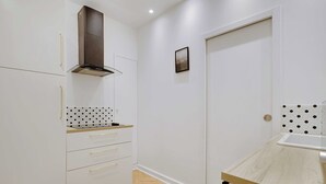 Cocina compacta con muebles blancos, encimera de madera y horno empotrado.