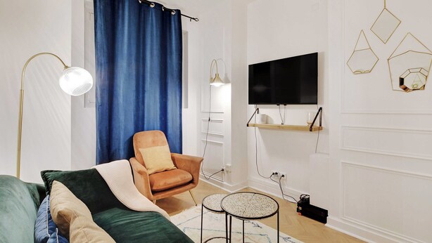 Una sala de estar moderna con un sofá verde, un sillón marrón, una cortina azul, un televisor de pantalla plana y decoración mural geométrica.