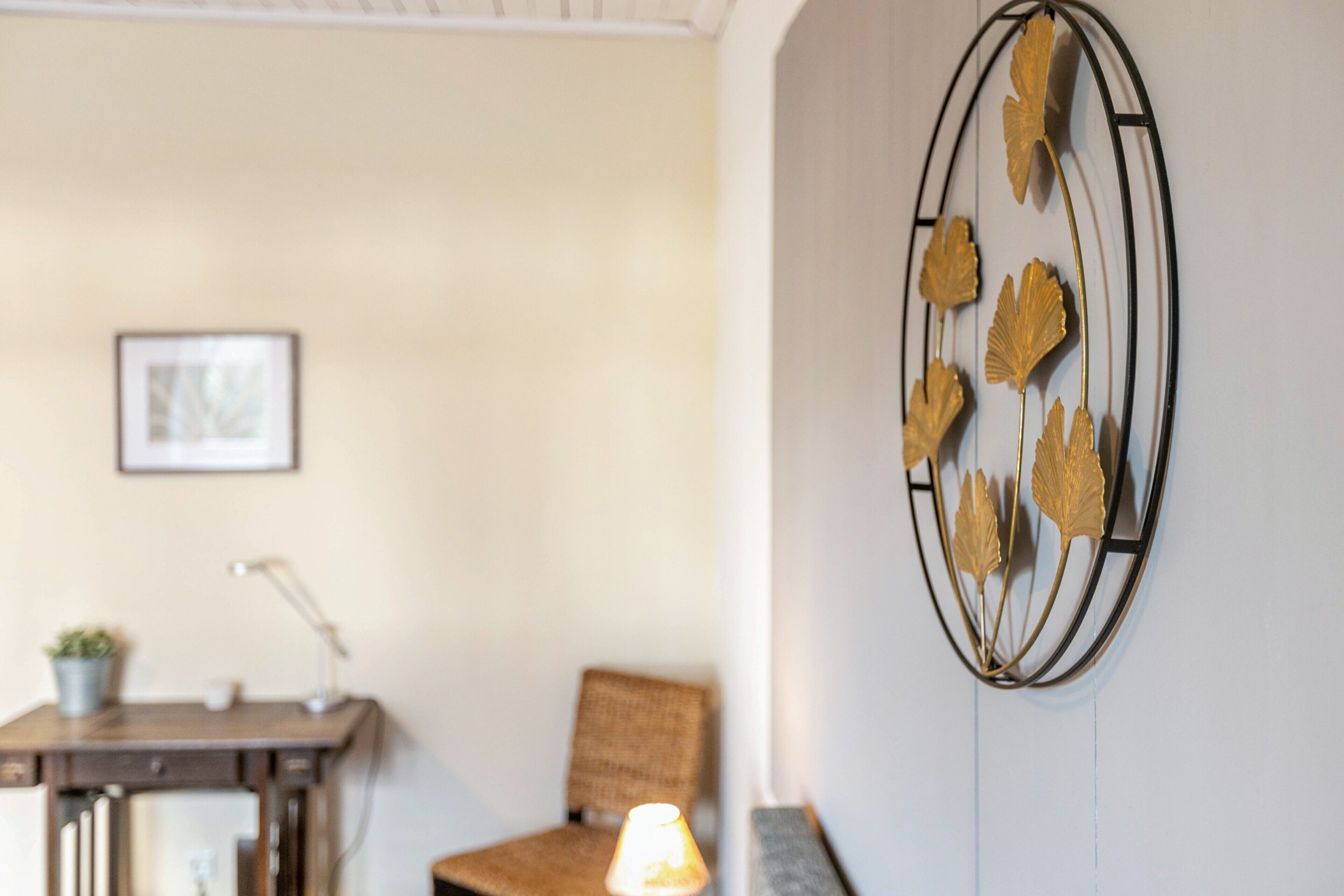 A room with a desk, chair, lamp, and a wall-mounted decorative piece.