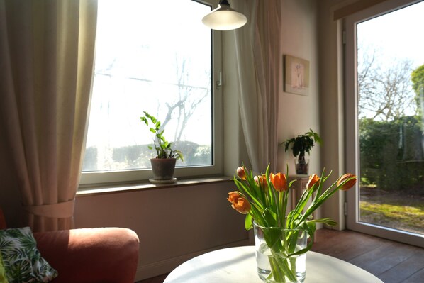 A room with a window, a potted plant, a vase with flowers, and a chair.