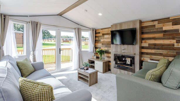 Een moderne woonkamer met een bank, een salontafel, een aan een houten wand bevestigde televisie en een open haard.