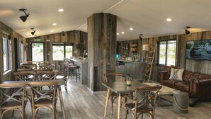Een eetgedeelte met houten stoelen en tafels, een bar met krukken, en een leren bank.