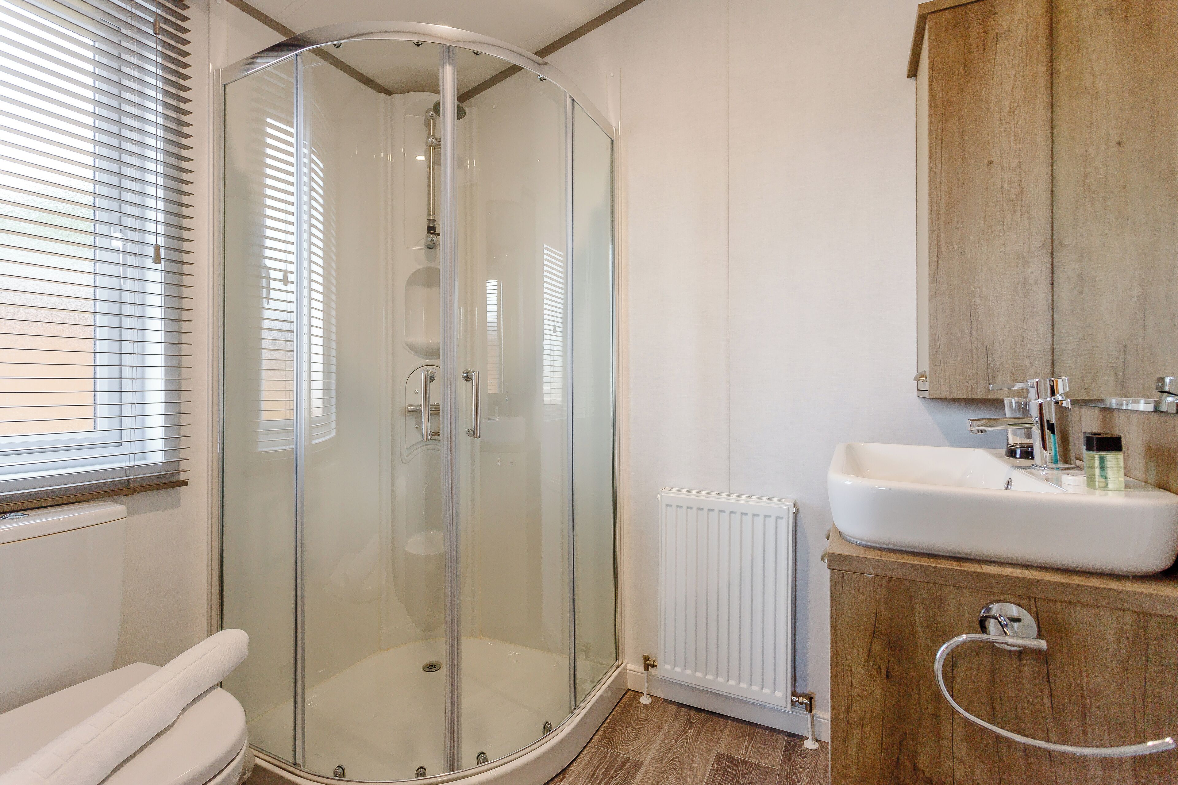 Een moderne badkamer met een douchecabine van glas, een witte wastafel en een houten kastje.