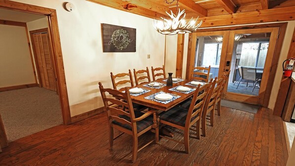 Uma sala de jantar com uma mesa de madeira posta para seis pessoas, rodeada por cadeiras de madeira.