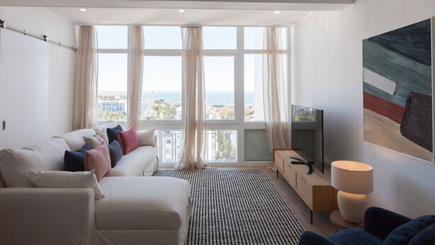 En moderne stue med sofa, fjernsyn og et stort vindue med gardiner.