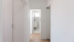En smal gang med hvide vægge og døre, der fører til et badeværelse med marmorgulv.