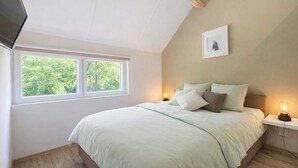 A bedroom with a large bed, a window, a bedside table with a lamp, and a framed picture on the wall.