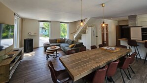 A spacious living area with a wooden dining table, comfortable seating, and a staircase leading to an upper level.