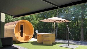 A wooden hot tub and a sauna in a circular wooden structure, with a patio table and chairs in the foreground.