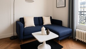 A modern living room with a dark blue sofa, a white floor lamp, and a small white table with decorative items. - 3 pieces pres du Pantheon (Paris)