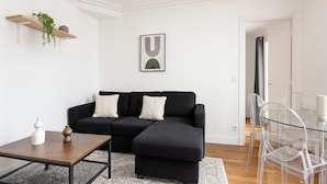 A modern living room with a black sectional sofa, a glass coffee table, and clear chairs. - 3 pieces pres du Pantheon (Paris)