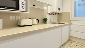 A modern kitchen with a microwave, toaster, and kettle on the counter, a small potted plant, and a window with a view. - 3 pieces pres du Pantheon (Paris)