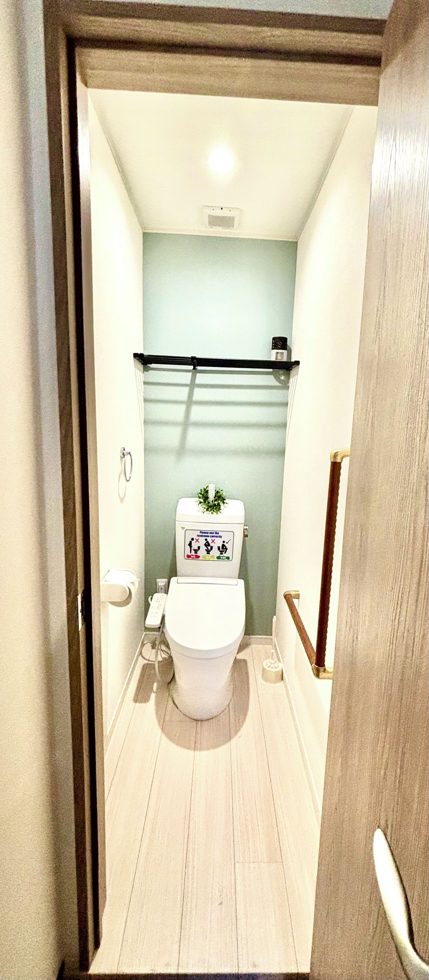 A narrow hallway leading to a bathroom with a toilet, a small shelf, and a light switch on the wall.