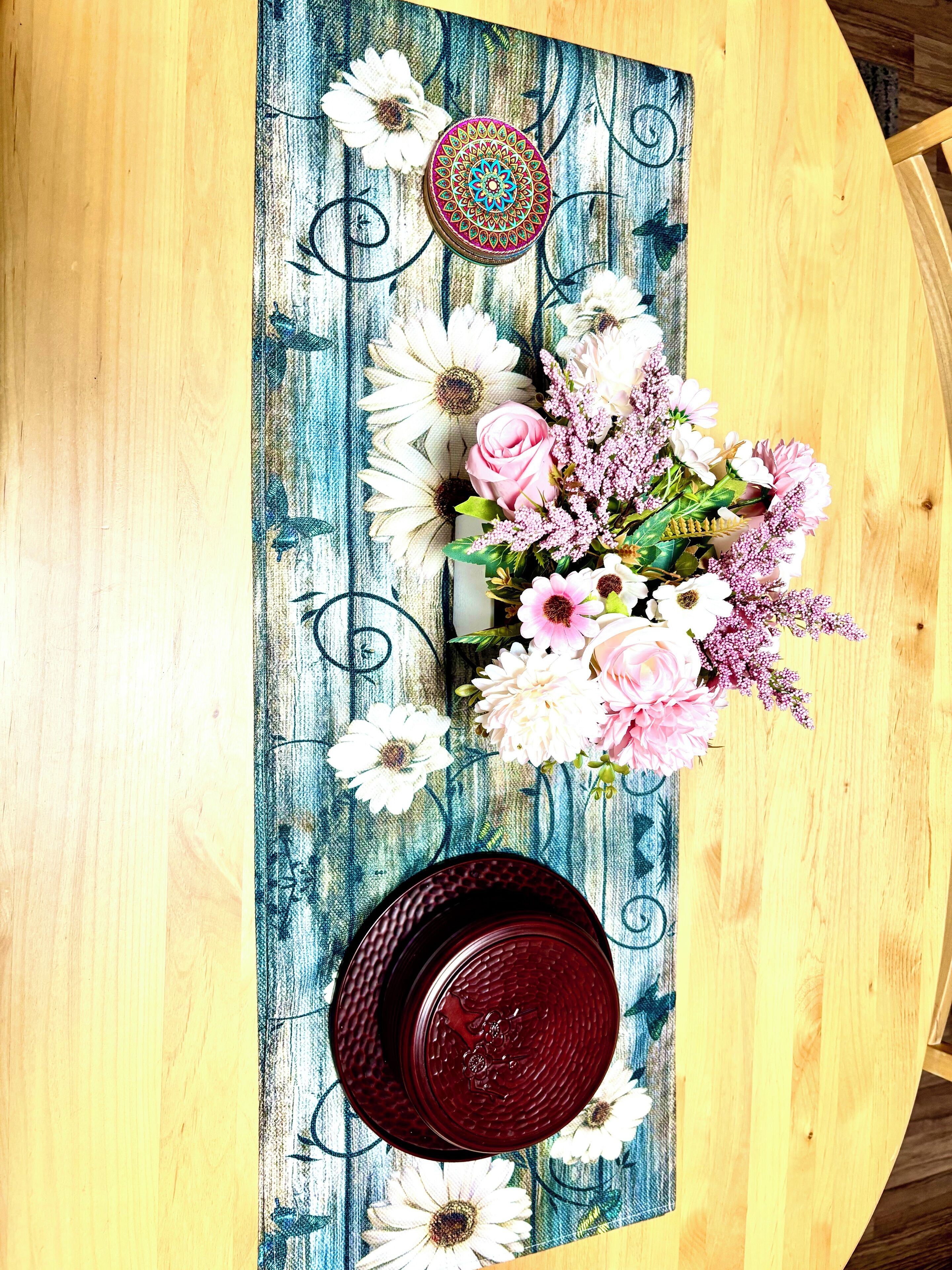A wooden table with a blue patterned tablecloth, a decorative plate, and a floral arrangement.
