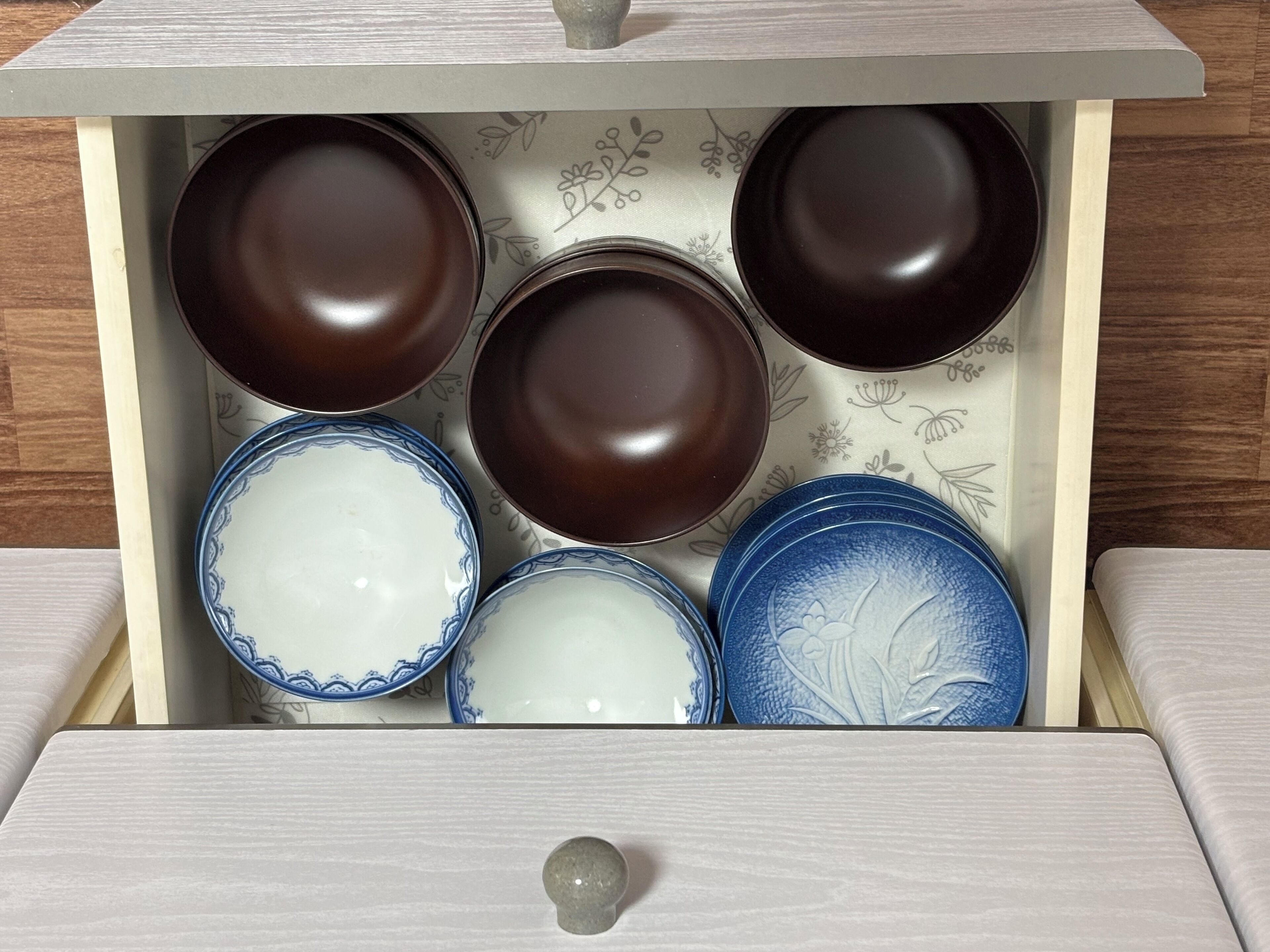 A drawer with six bowls, three dark brown and three white with blue patterns.