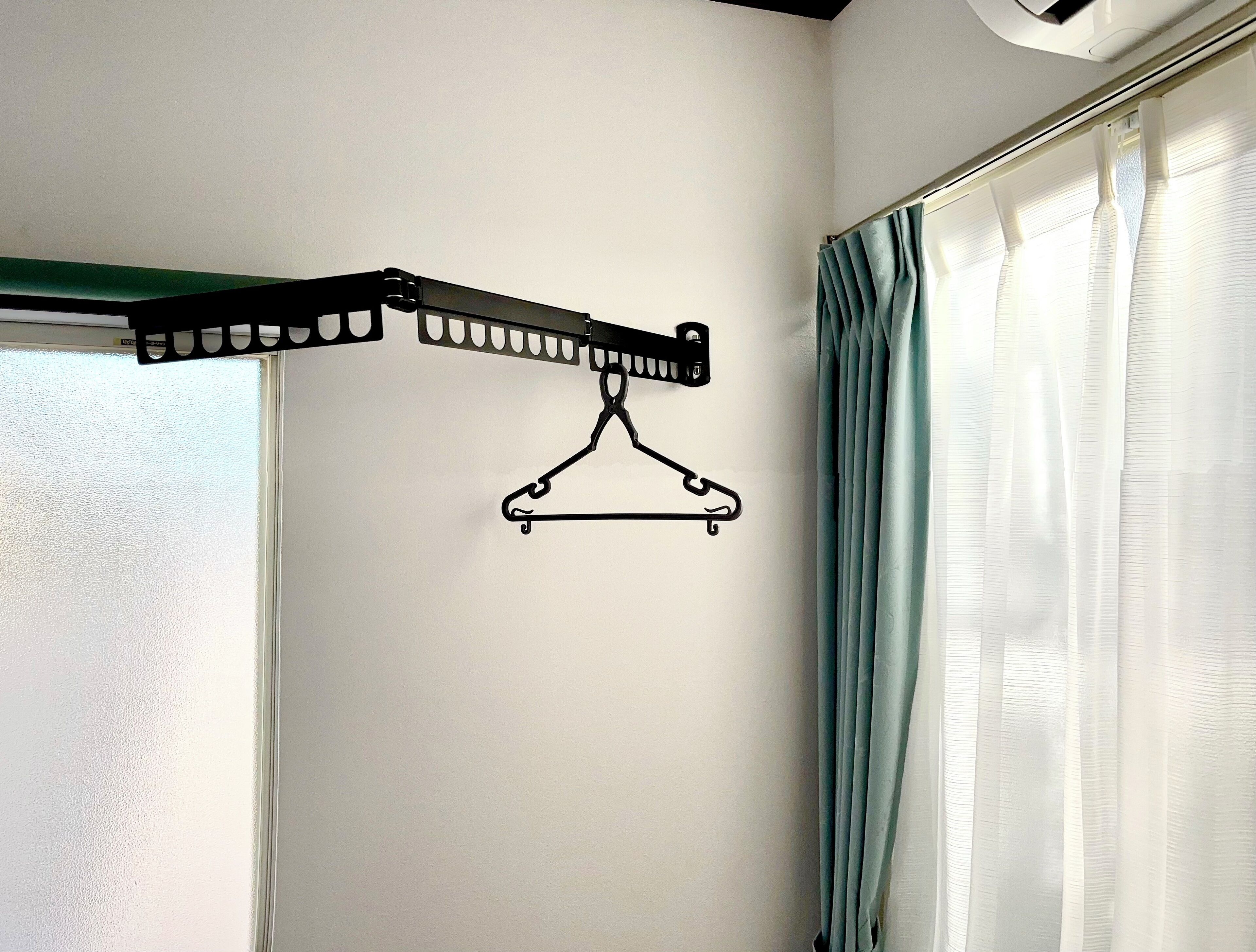 A room with a black metal drying rack mounted on a white wall, a window with white curtains, and a door with a frosted glass panel.