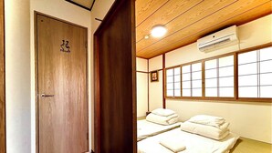 A hotel room with a wooden door marked "TOILET," a bed with white bedding, a window with grid panes, and an air conditioning unit on the ceiling. - Happy Inn Kyoto  en-no-yado (Kyoto)