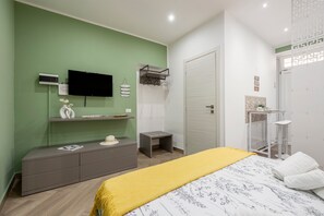 Quarto com cama, cômoda, televisão, mesinha e porta.
