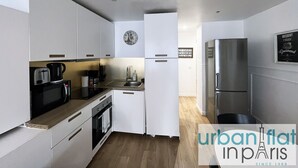 Une cuisine moderne avec des meubles blancs, un réfrigérateur en acier inoxydable, une horloge et un panneau affiché sur le mur.