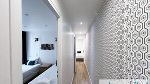 Un couloir d’hôtel moderne avec un mur orné de motifs, un lit recouvert de draps blancs et un plancher en bois.