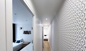 A modern hotel corridor with a patterned wall, a bed with white linens, and a wooden floor. - Urban Flat 14 - Charming 3 BDR Flat in Paris (París)