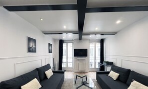 A modern living room with two black sofas, a glass coffee table, and a flat-screen TV mounted on the wall. - Urban Flat 14 - Charming 3 BDR Flat in Paris (París)