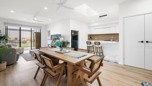 A modern kitchen with white cabinets, a wooden dining table, and a ceiling fan.