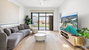 A modern living room with a grey sofa, a round white coffee table, and a flat-screen TV on a wooden stand.