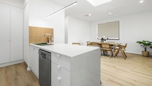 A modern kitchen with a built-in dishwasher, a wooden accent wall, and a dining area with a table and chairs.
