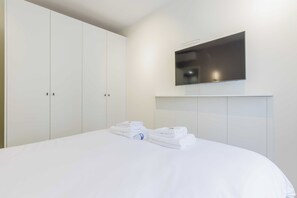 A hotel room with a large bed, a flat-screen TV mounted on the wall, and a wardrobe with multiple doors. - Cozy Apartment 2br/6p - Sacre-coeur / Montmartre (Paris)