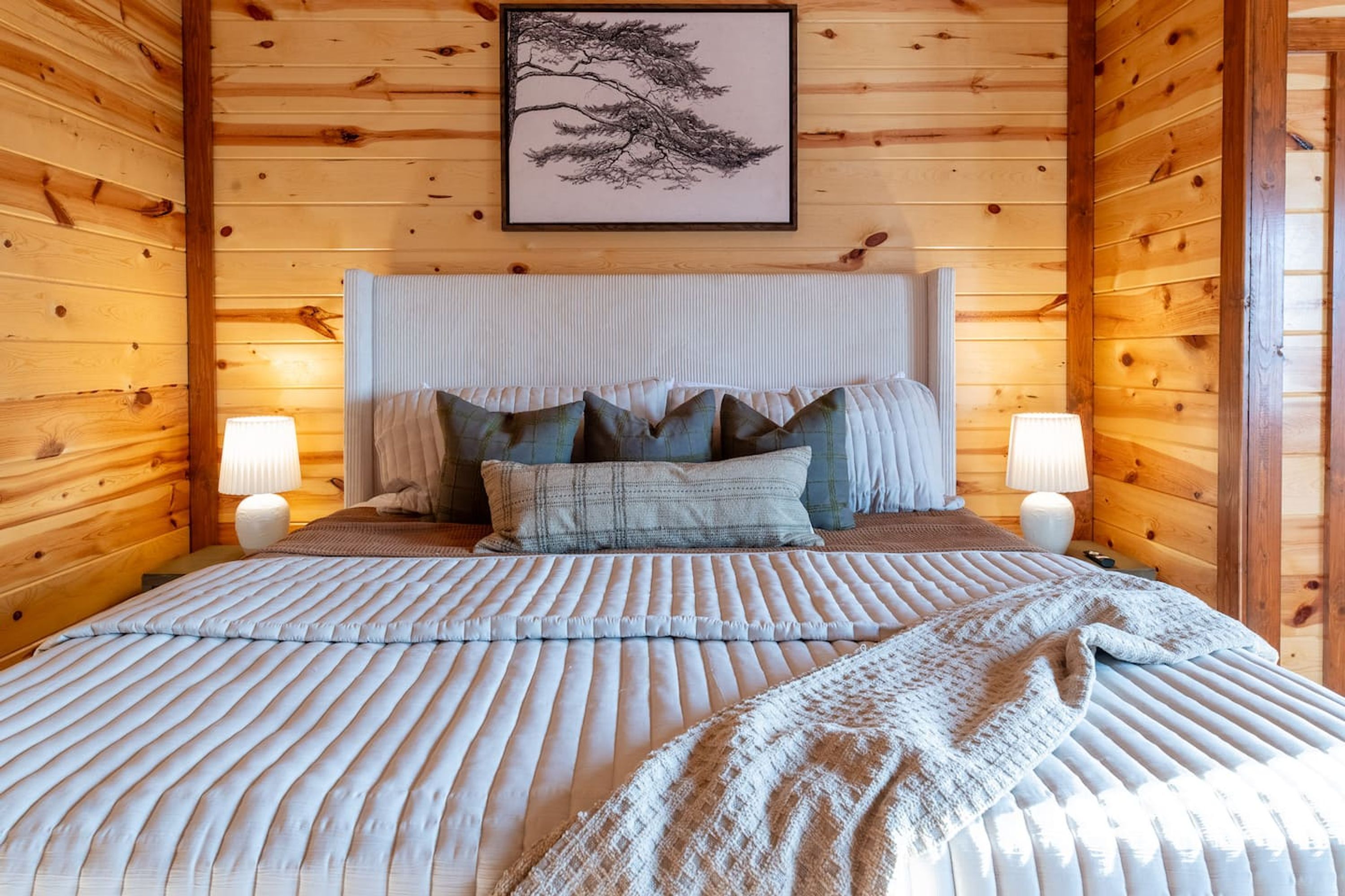 Une chambre aux murs lambrés, avec un lit, des oreillers et deux lampes de chevet.