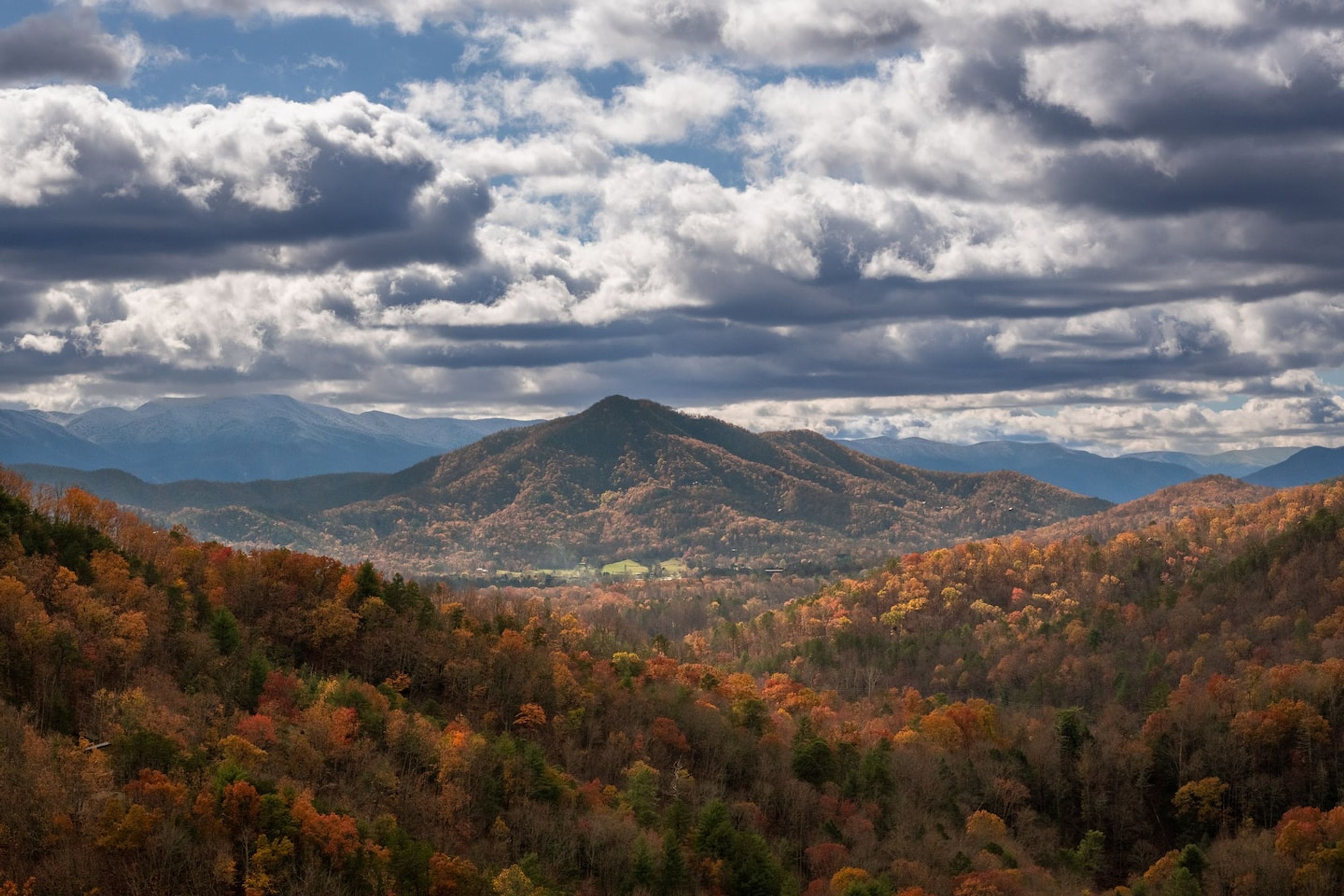 A mountainous landscape with autumn foliage and a cloudy sky.