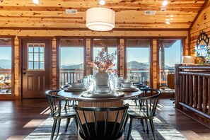A wooden interior with a round dining table set for six, surrounded by chairs, and a view of mountains through large windows. - Pet-friendly Pool Game Room Hot Tub Theater (Sevierville)