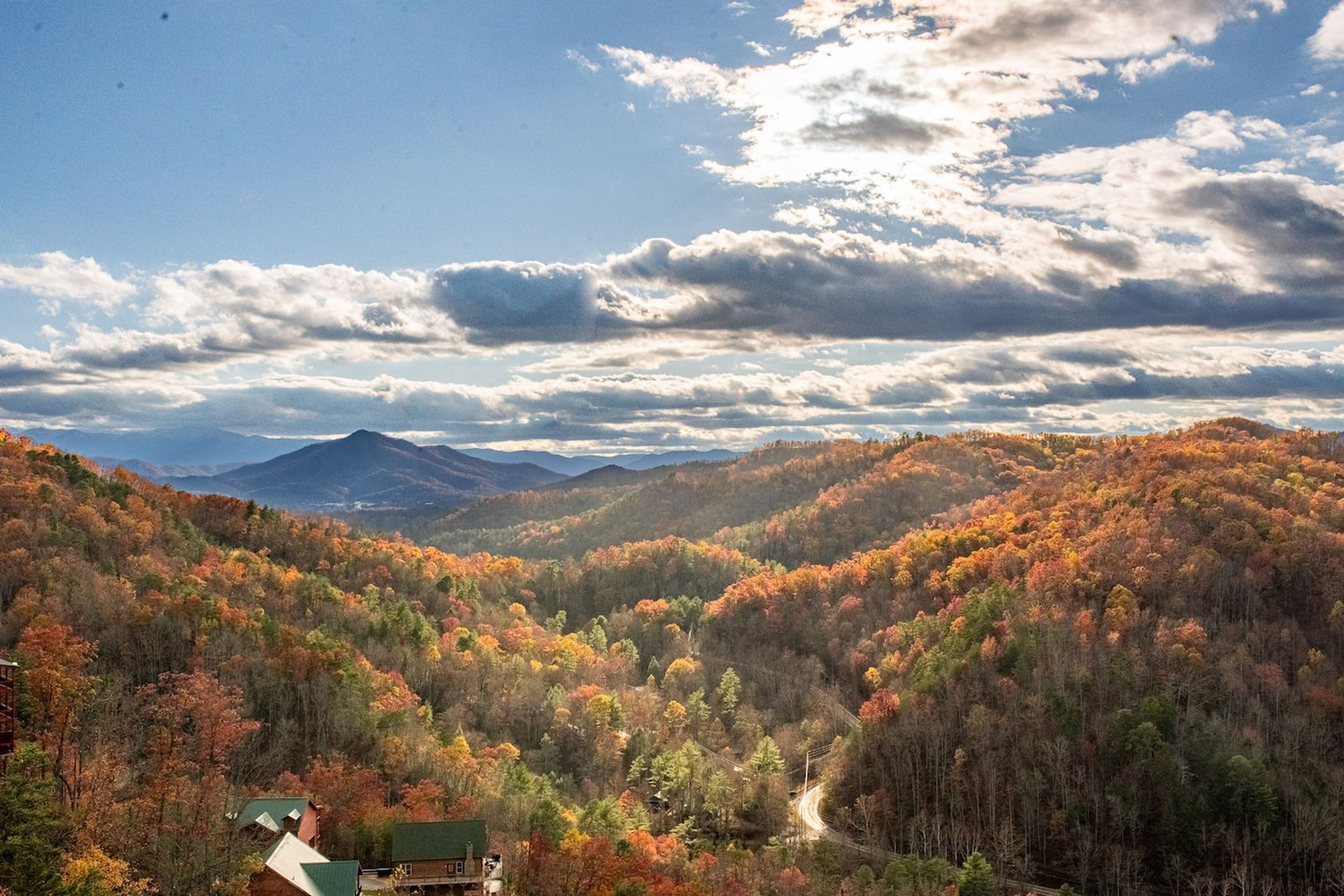 A mountainous landscape with autumn foliage, a winding road, and a building with a green roof.