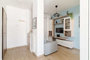 A modern living room with a TV, shelving, and a grey ottoman.