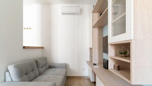 A modern living room with a grey sectional sofa, built-in wooden shelving, and a wall-mounted air conditioner. - GuestHost - Naviglio Grande Bright Apartment (Milan)