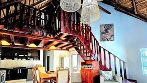 A spacious living area with a wooden staircase, a dining set, and hanging light fixtures.
