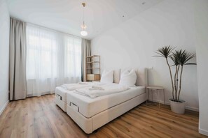Une chambre moderne avec un grand lit, un plancher en bois, une petite table de chevet et une plante en pot.