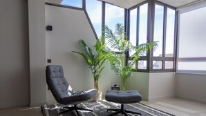 Ein modernes Wohnzimmer mit einem großen Fenster, zwei grauen Sesseln, einem gemusterten Teppich und einer Zimmerpflanze.
