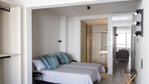 Ein modernes Hotelzimmer mit einem Doppelbett, einem kleinen Schreibtisch und einem Stuhl. Ein Badezimmer ist durch eine offene Tür sichtbar.