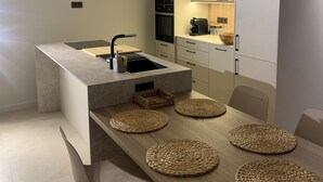 Eine moderne Küche mit Kochinsel, integrierten Geräten und einem Essbereich mit Holztisch und gewebten Unterlagen.