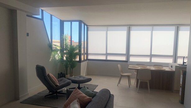 Ein modernes Wohnzimmer mit Sofa, Sessel und Essbereich mit Tisch und Stühlen.