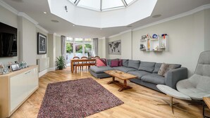 Een ruime woonkamer met een groot dakraam, een grijze bank, een houten salontafel en een kleurrijk tapijt.