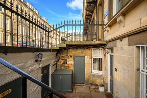 A narrow alleyway with a metal fence, a small utility box, and a door to a building.