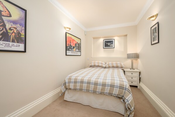 A bedroom with a bed, a nightstand, a lamp, and wall art including a poster and a framed picture.