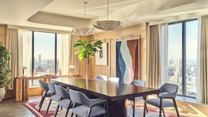 A modern conference room with a large table, chairs, a potted plant, and large windows offering a city view.