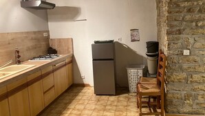 Keittiössä on puukaapit, kaasuliesi, jääkaappi, roskakori ja kiviseinä.