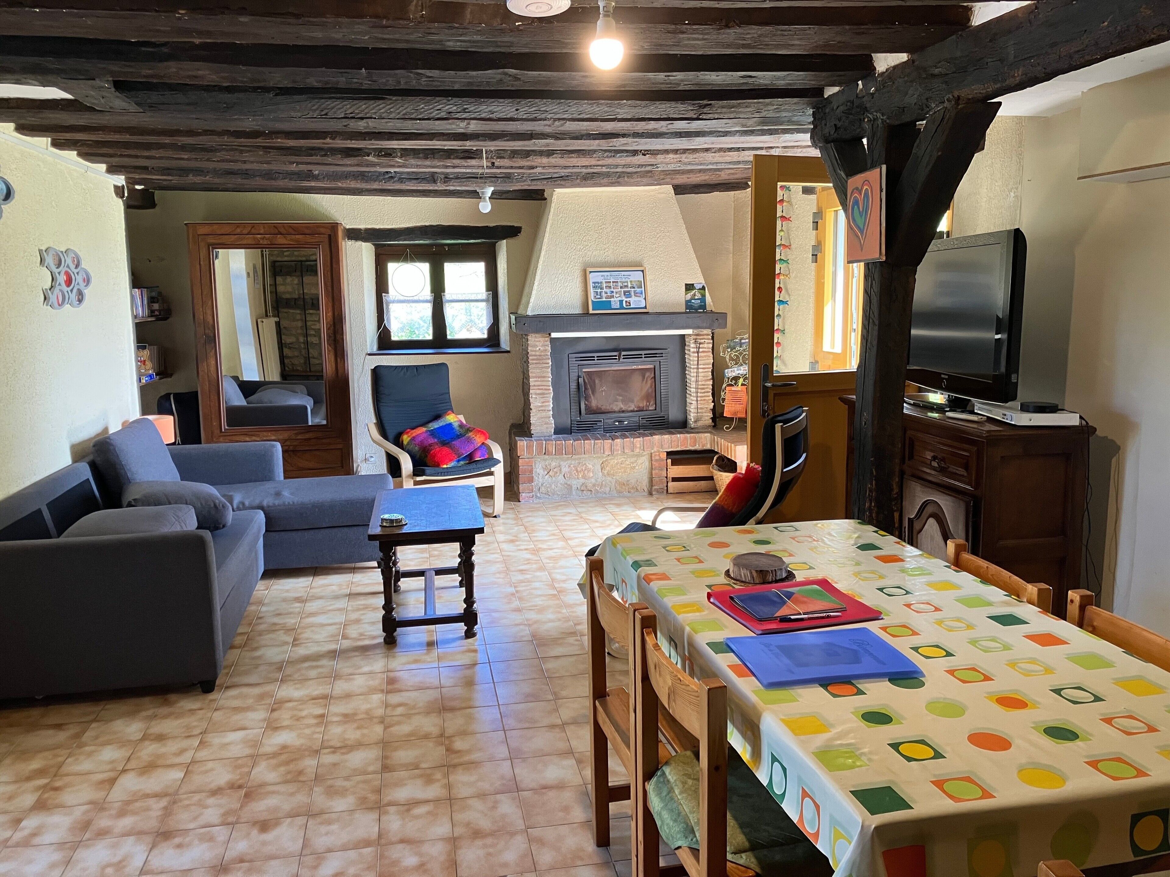 Een gezellige woonkamer met een open haard, een televisie en een eethoek met een kleurrijk tafelkleed.